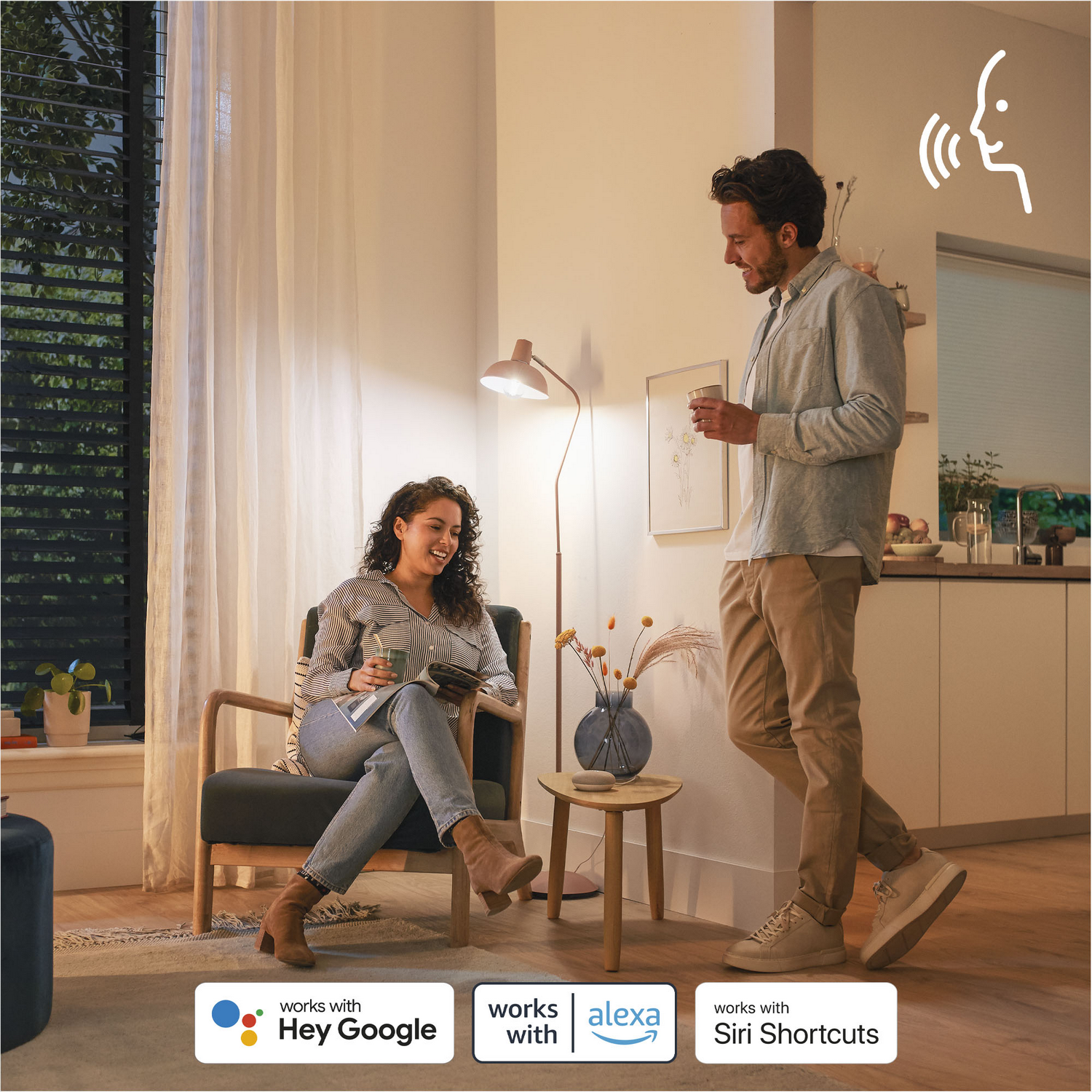 Un hombre y una mujer en una habitación, la mujer está sentada y sonríe. El hombre está de pie, también sonriendo.