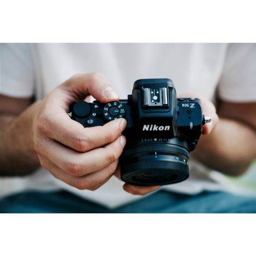 Una persona sostiene una cámara Nikon negra. Las manos están cerca de la cámara, enfocándose en los botones y la lente.