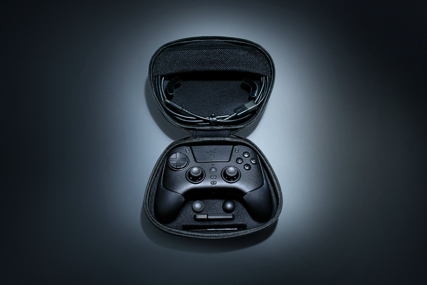 Mando de juegos negro, auriculares y accesorios dentro de una funda negra abierta sobre un fondo degradado.
