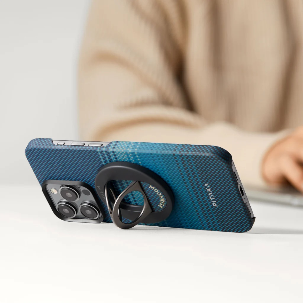 Niebieski telefon w kratę z uchwytem na pierścień leży na stole.