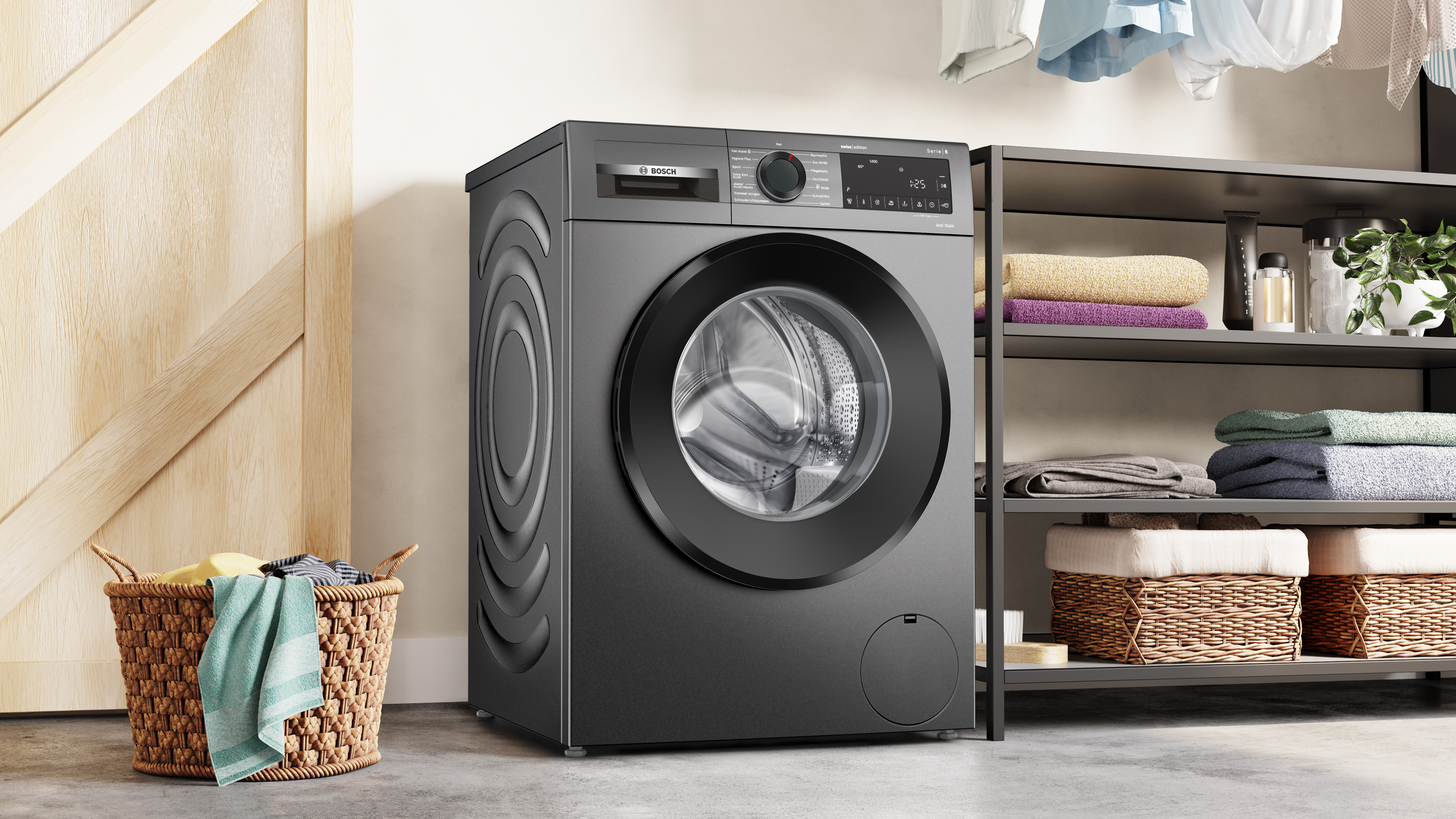 Un lave-linge noir est dans une buanderie. Un panier de linge est devant. Des étagères avec des serviettes sont à droite.