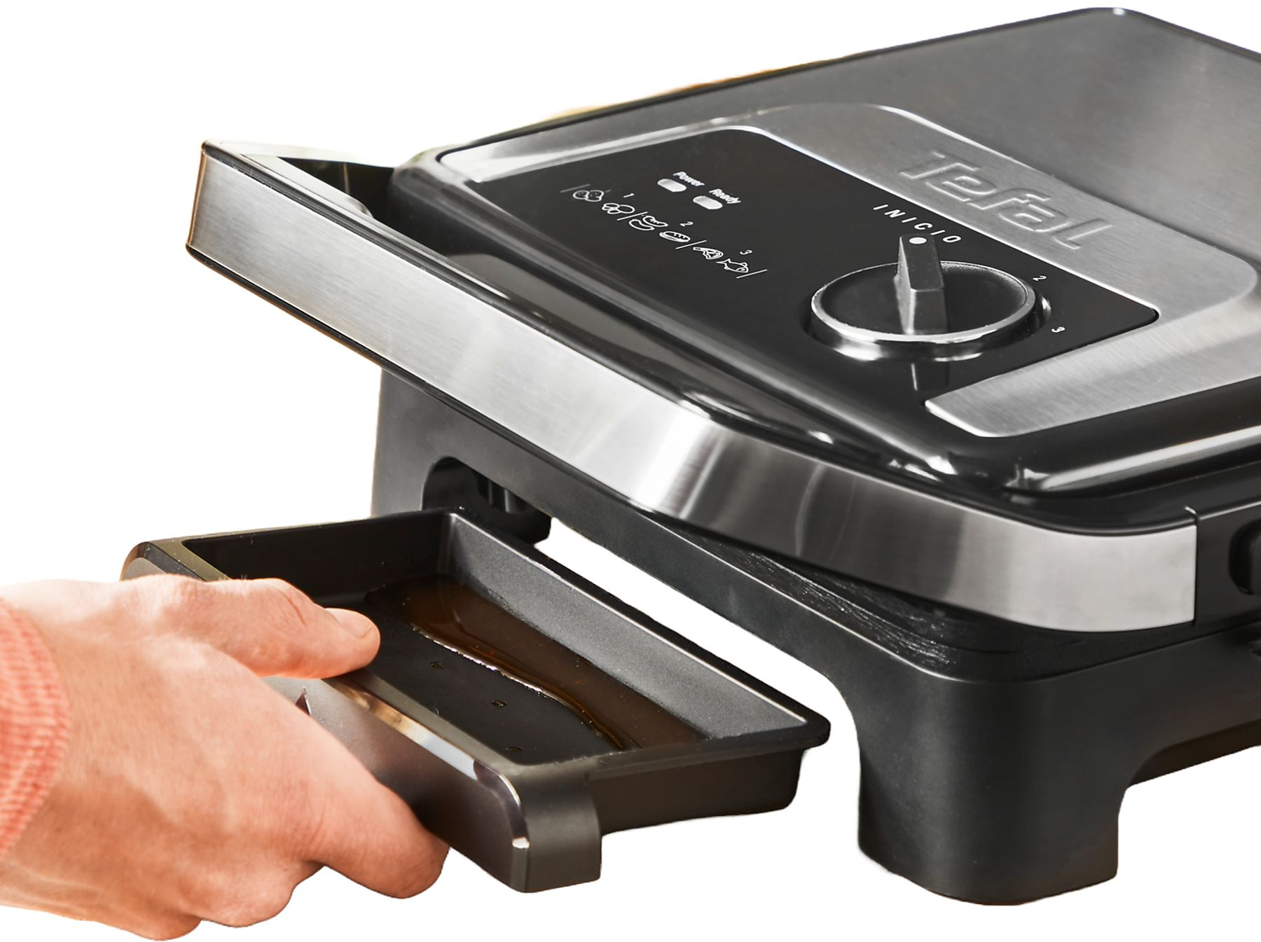 Eine Person hält eine schwarze Schale von einem Tefal-Grill. Der Grill ist schwarz und silber mit einem Drehknopf und Bedienfeld.