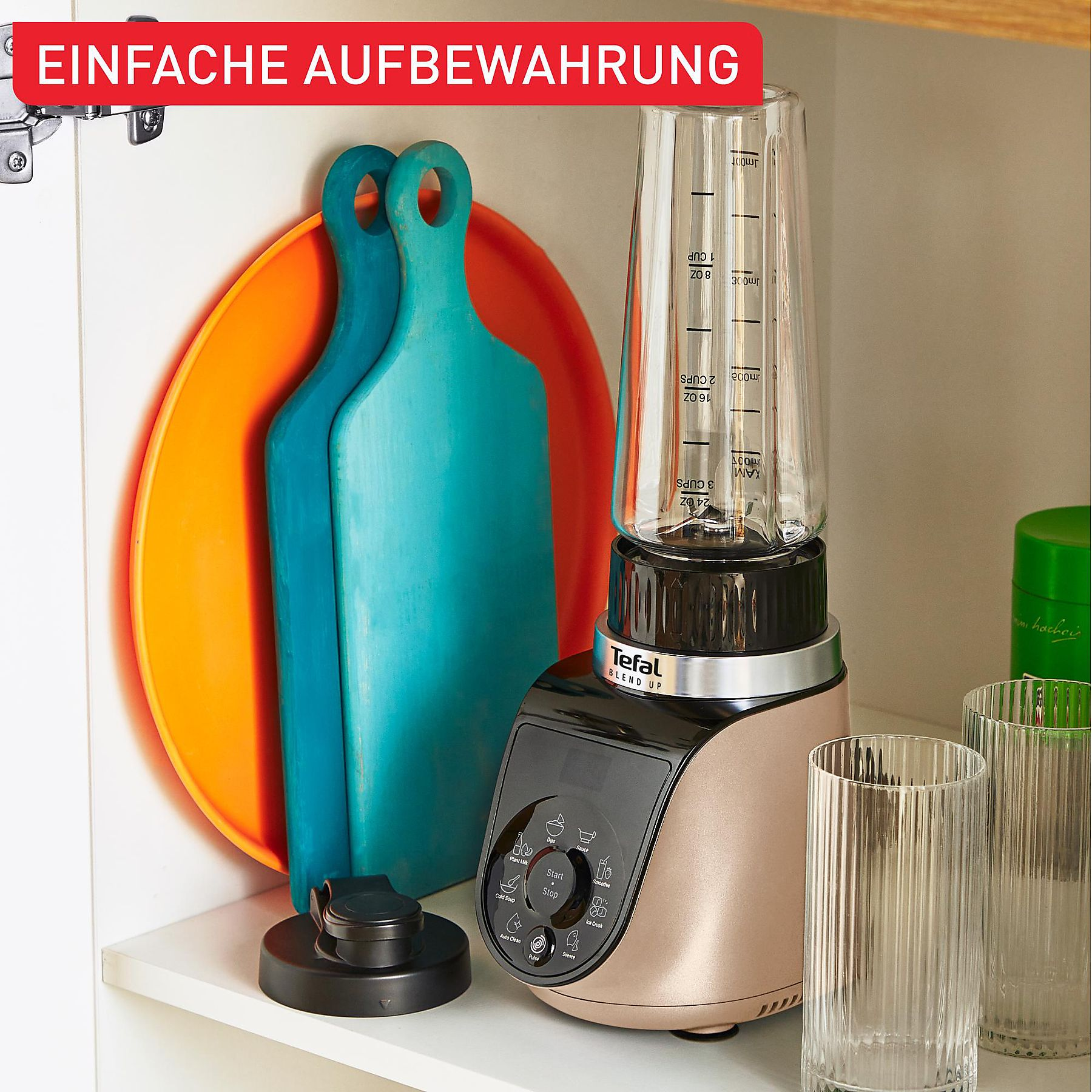 Ein Mixer mit Messbecher, Schneidebrettern und Gläsern steht auf einem Regal. Eine Schranktür mit Text oben.