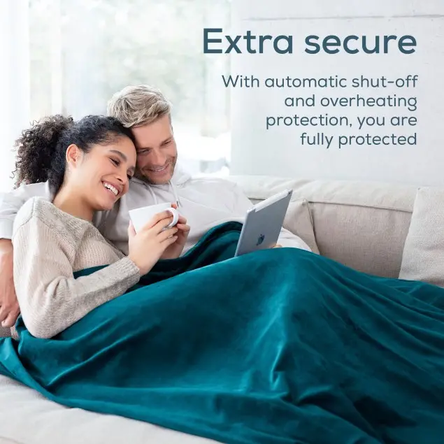 Una coppia seduta su un divano sotto una coperta turchese, guarda un tablet. Uno tiene una tazza. Il testo dice 'Extra sicuro'.
