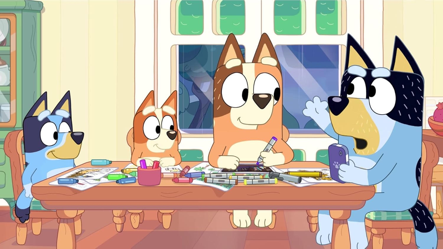 Quattro cani dei cartoni animati a un tavolo. Uno tiene un telefono, altri disegnano e colorano. Una finestra e degli armadi sullo sfondo.