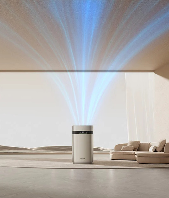 Oczyszczacz powietrza emituje niebieskie prądy powietrza. Beżowy pokój, sofa po prawej i pustynne tło są widoczne.