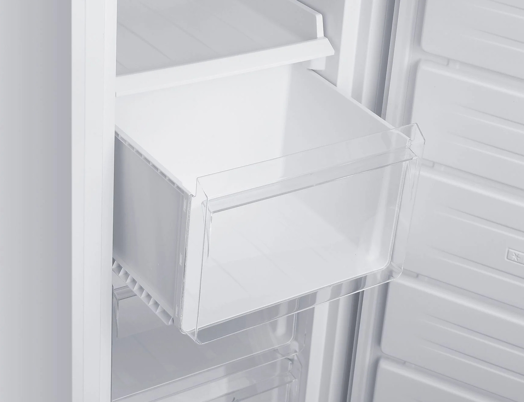 Wewnątrz białej lodówki, przezroczysta szuflada jest otwarta. Widoczne są inne białe przegrody.