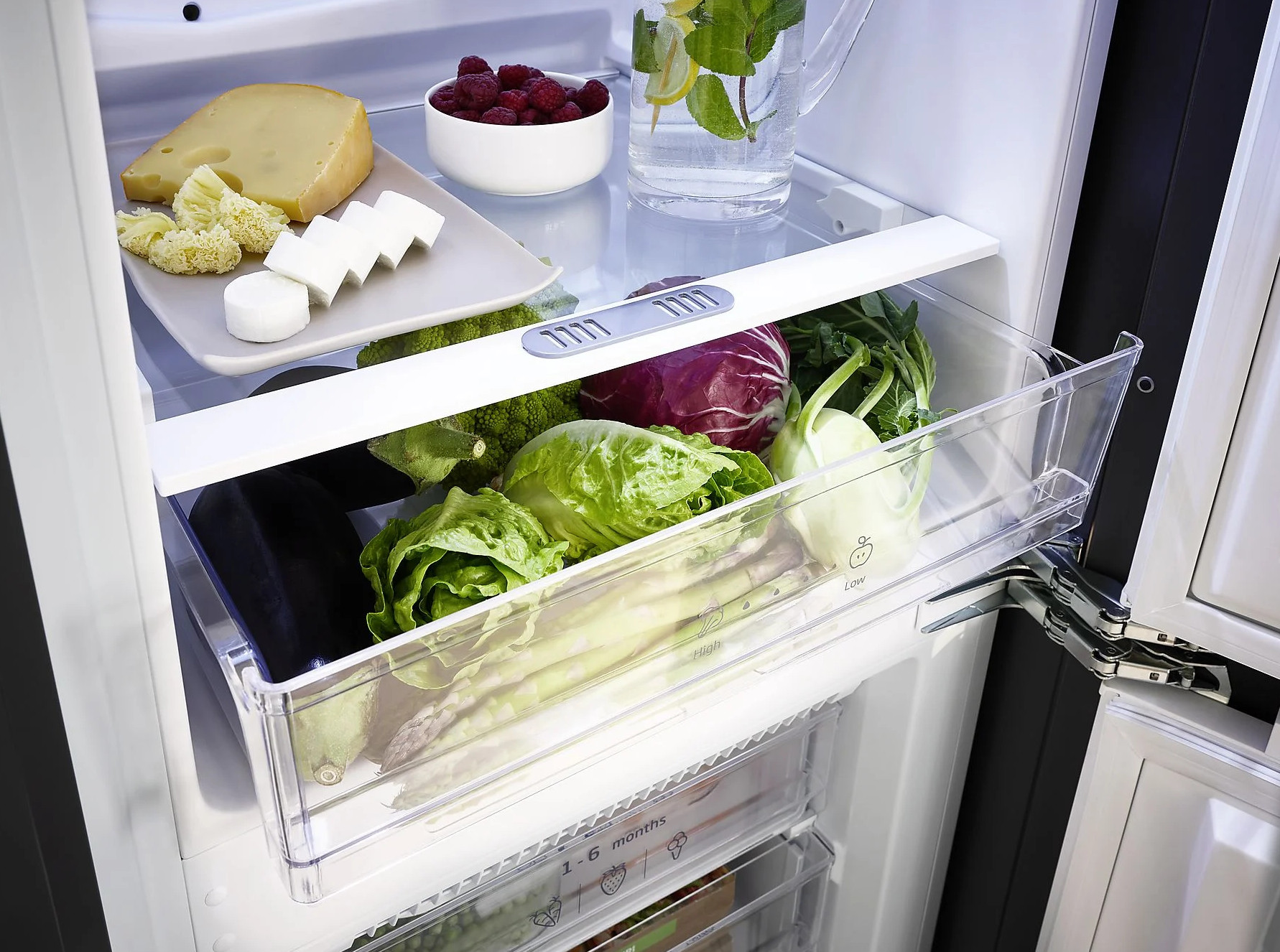 W lodówce: ser, jagody, warzywa i dzbanek z wodą z cytryną i miętą. Przechowywane różne produkty.