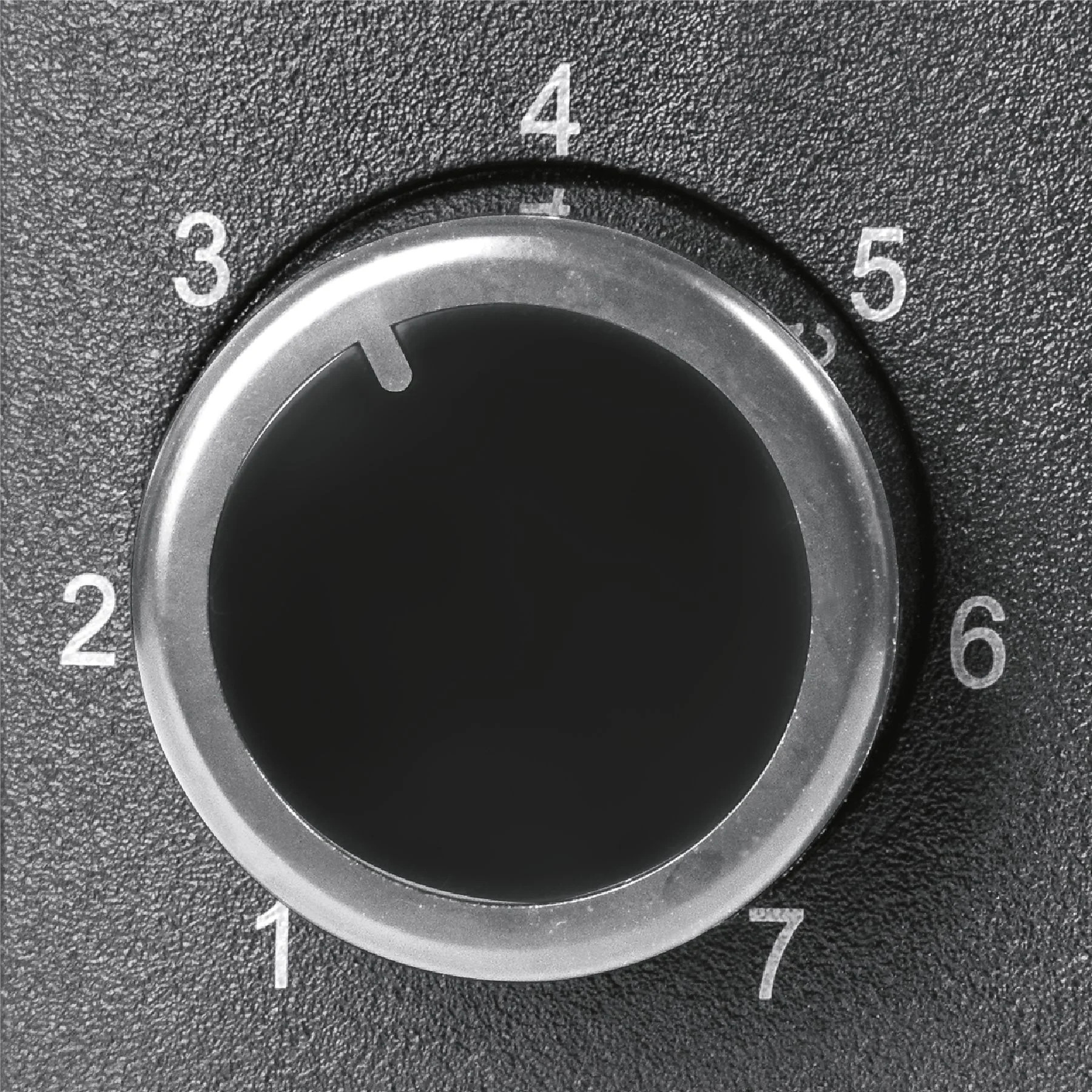 Zbliżenie czarnego pokrętła z białymi cyframi od 1 do 7. Srebrny pierścień otacza czarne centrum. Tło jest teksturowane.