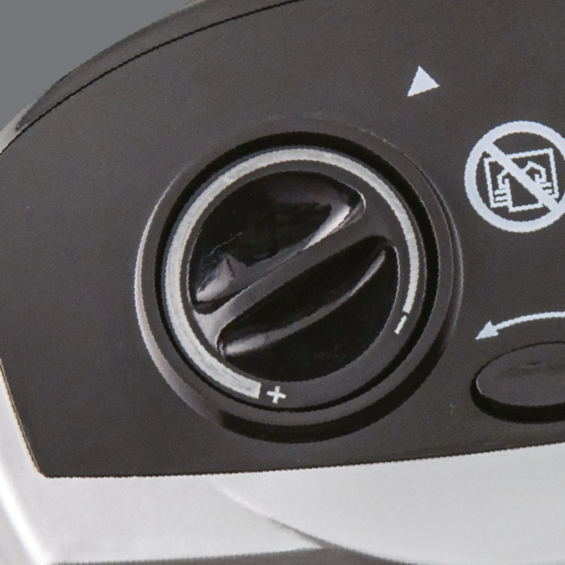 Zbliżenie czarnego pokrętła z symbolami plus i minus. Widoczny jest biały trójkąt i symbol zakazu.