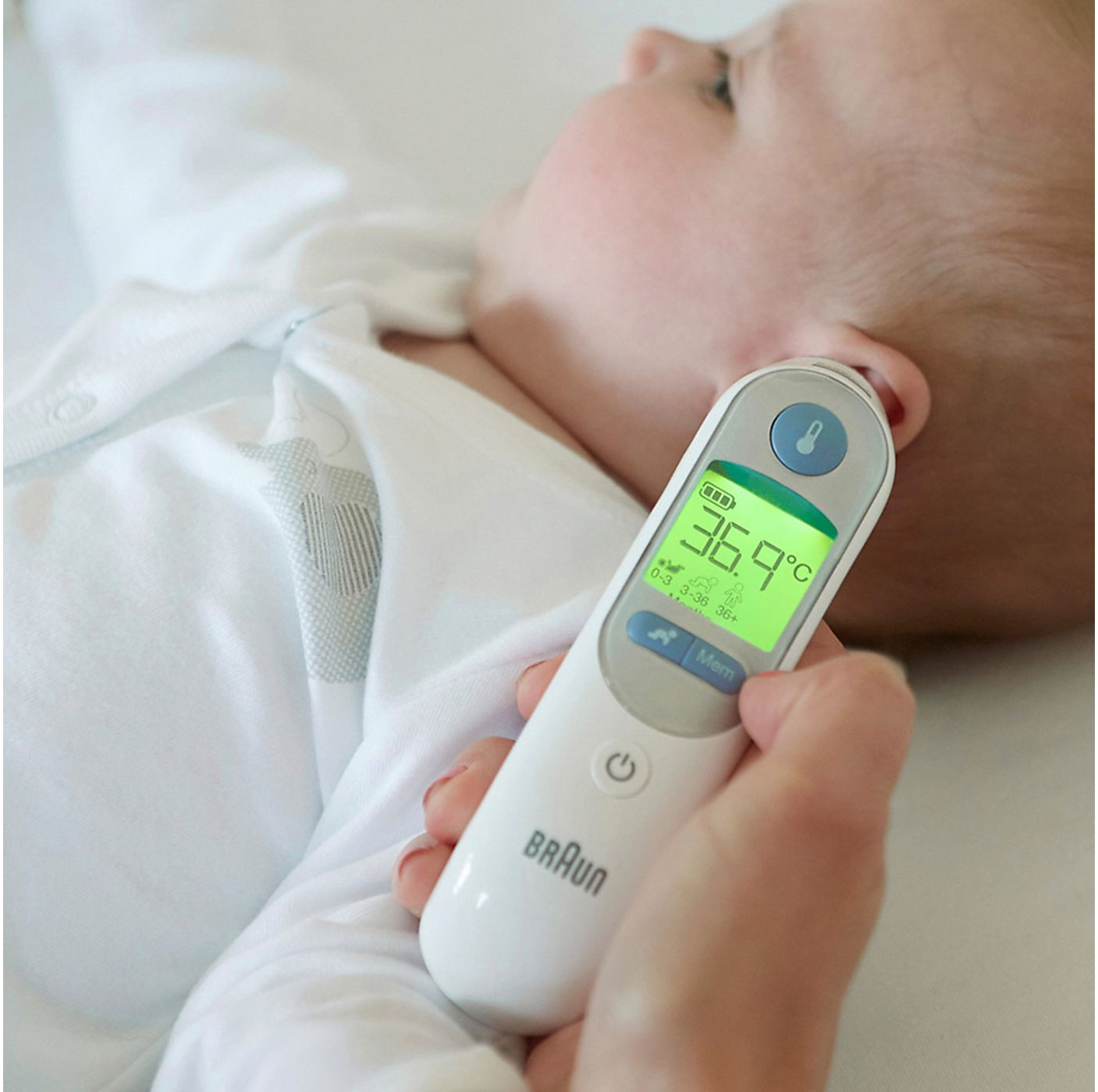 L'orecchio di un bambino viene controllato con un termometro Braun. Il termometro mostra 36,9°C. Il bambino indossa abiti bianchi.