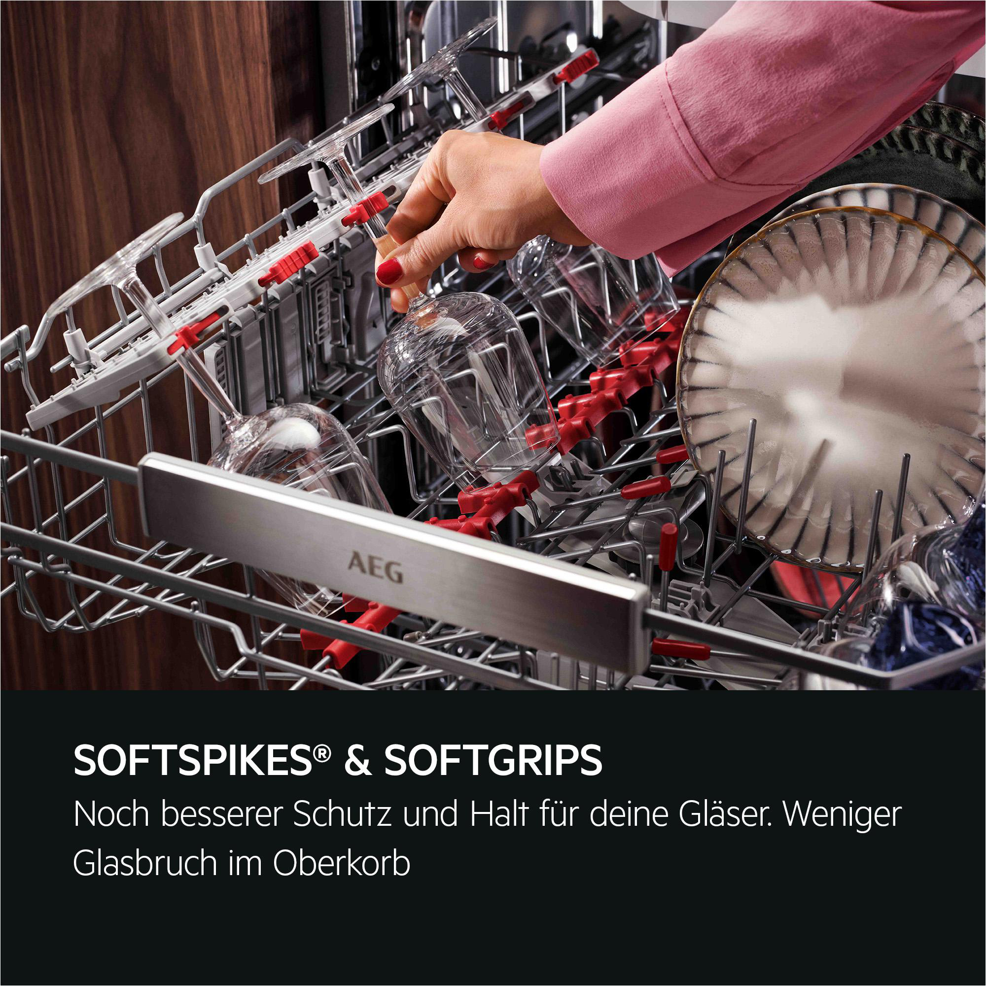 Eine Hand platziert ein Glas in einer Spülmaschine. Die Spülmaschine hat rote Griffe. Ein Teller ist sichtbar. Rosa Ärmel.