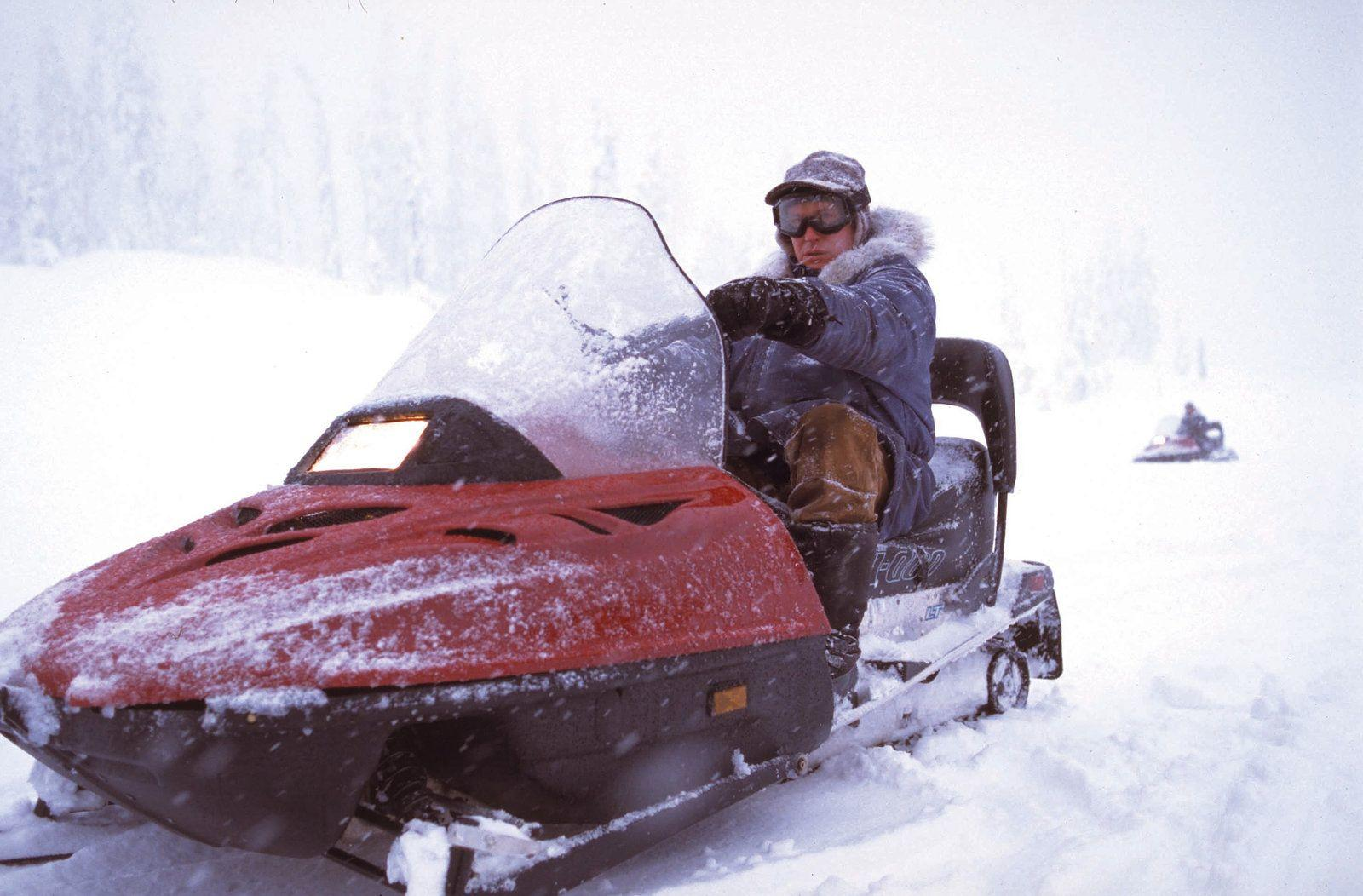 Eine Person in Winterkleidung fährt mit einem rot-schwarzen Motorschlitten durch eine verschneite Landschaft.