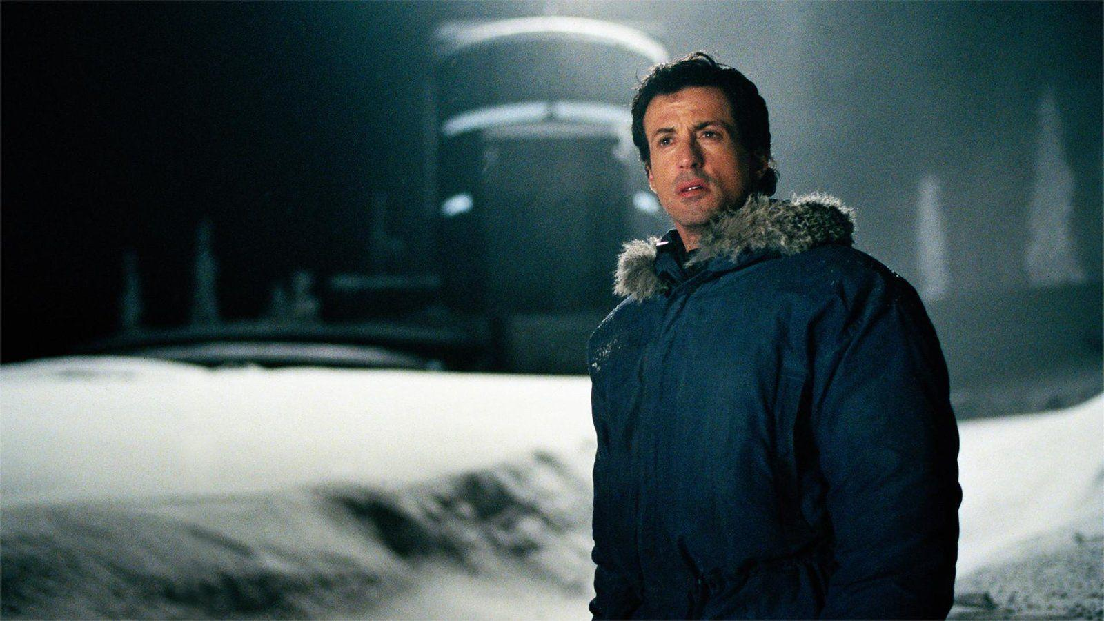 Ein Mann in einem blau gefütterten Parka steht in einer verschneiten, dunklen Umgebung mit unscharfen Lichtern.