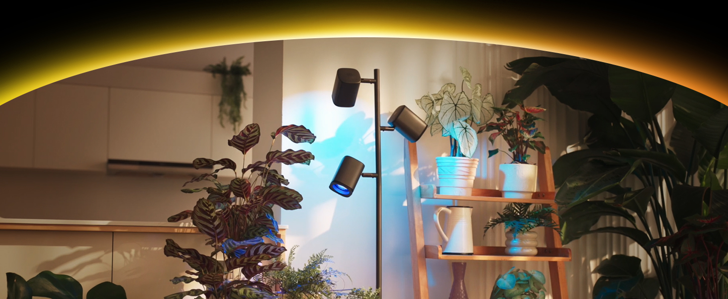 Ein moderner Stehlampe mit drei Spots beleuchtet Pflanzen in einem Raum.