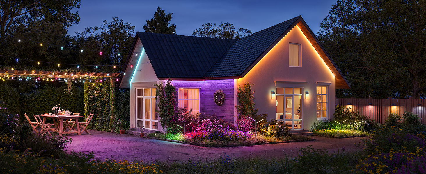 Ein Haus, beleuchtet von bunten Smart Lights in der Dämmerung, mit Gartentisch und Stühlen.