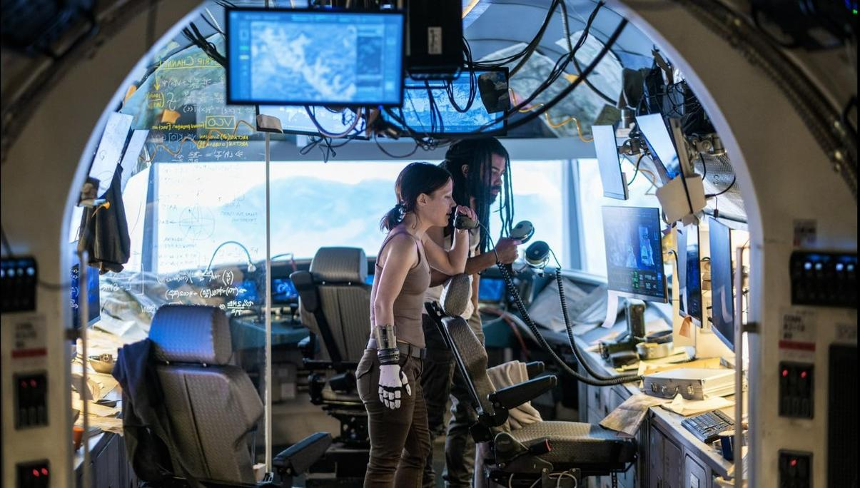 Zwei Personen in einem Raumschiff-Cockpit mit Bildschirmen und Formeln an der Wand.