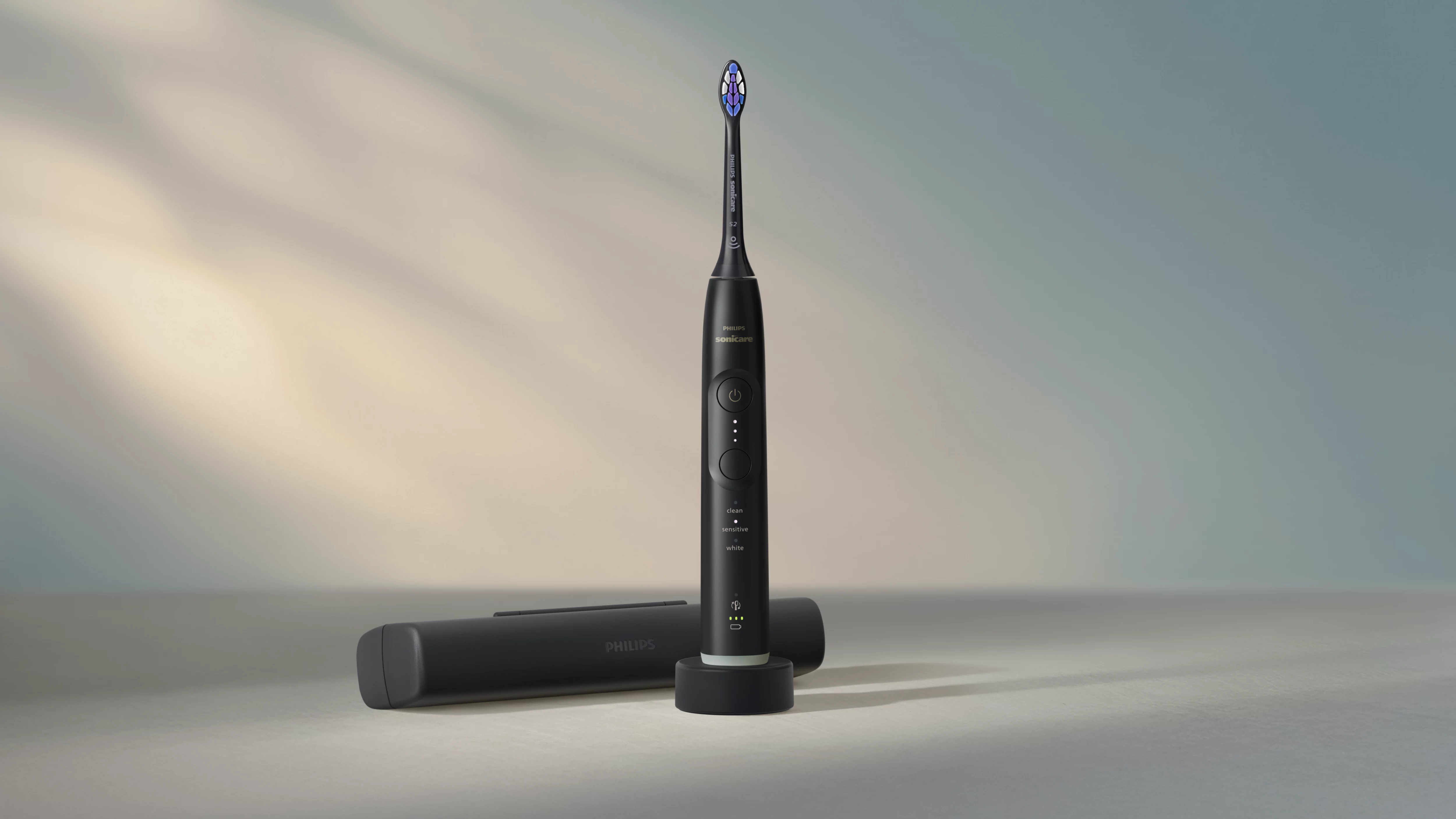 Schwarze Philips Sonicare Zahnbürste auf Ladegerät mit Reiseetui daneben.