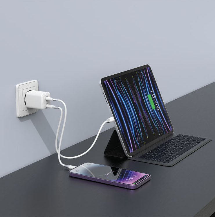 Un caricabatterie bianco alimenta un tablet e un telefono su una scrivania scura.