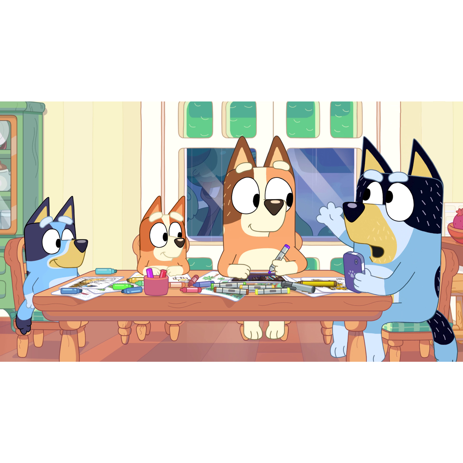 Four dogs sit at a table drawing with crayons and markers. One dog holds a phone.