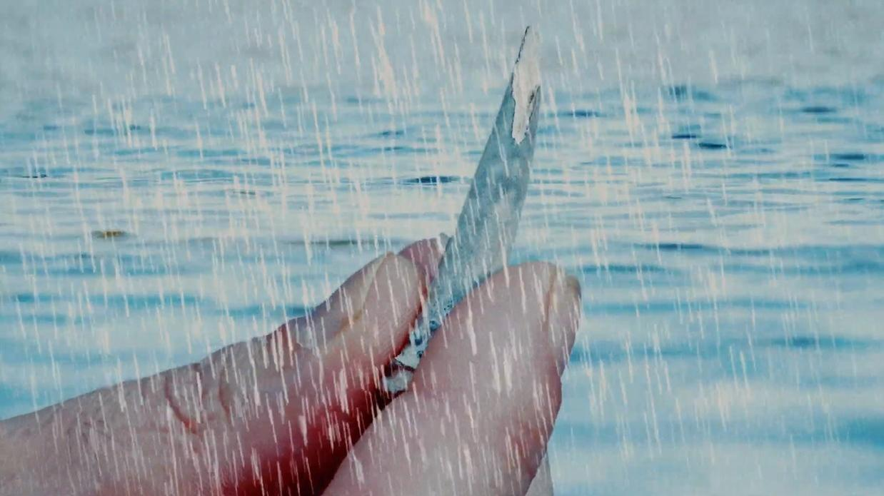 Eine Hand hält ein kleines Objekt vor einem blauen, regnerischen Hintergrund.