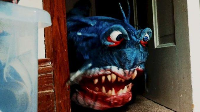 Eine gruselige blaue Monster-Maske mit scharfen Zähnen und roten Augen lugt hinter einer Tür hervor.