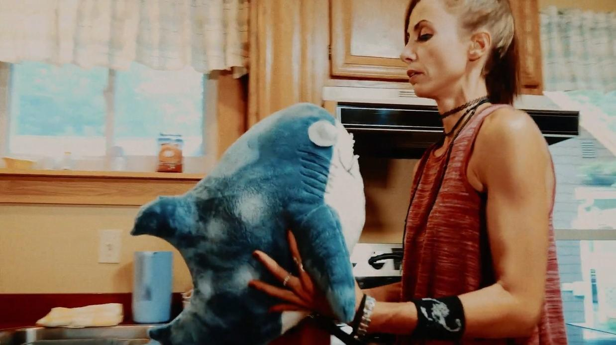 Eine Frau in einem roten Tanktop hält ein blaues Hai-Plüschtier in einer Küche.