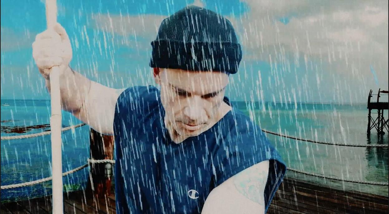 Mann mit Mütze im Regen am Meer, hält sich an einem Seil fest.