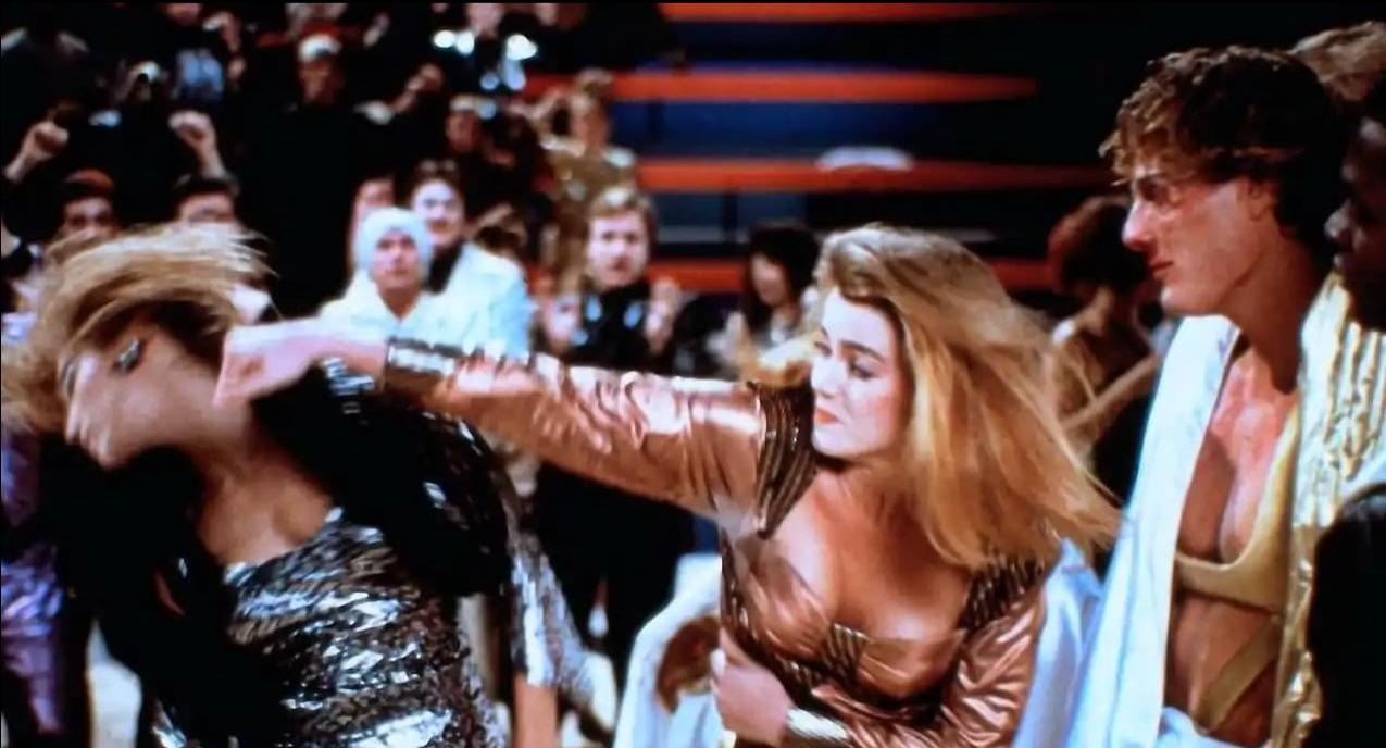 Eine Frau im goldenen Outfit schlägt eine Frau in einem glitzernden Kleid.