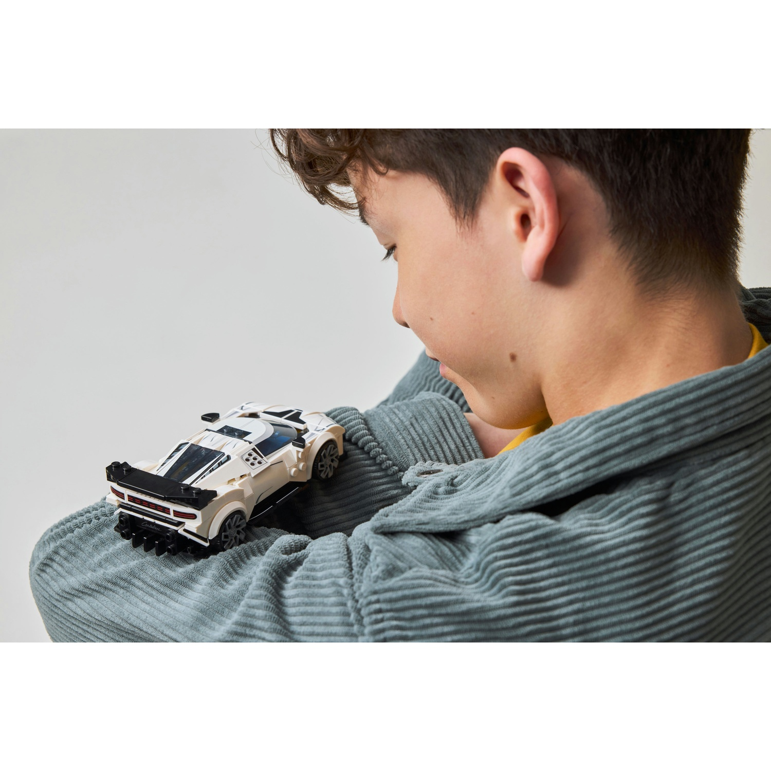 Un ragazzo tiene in mano un'auto Lego bianca e nera appoggiata sul maglione.