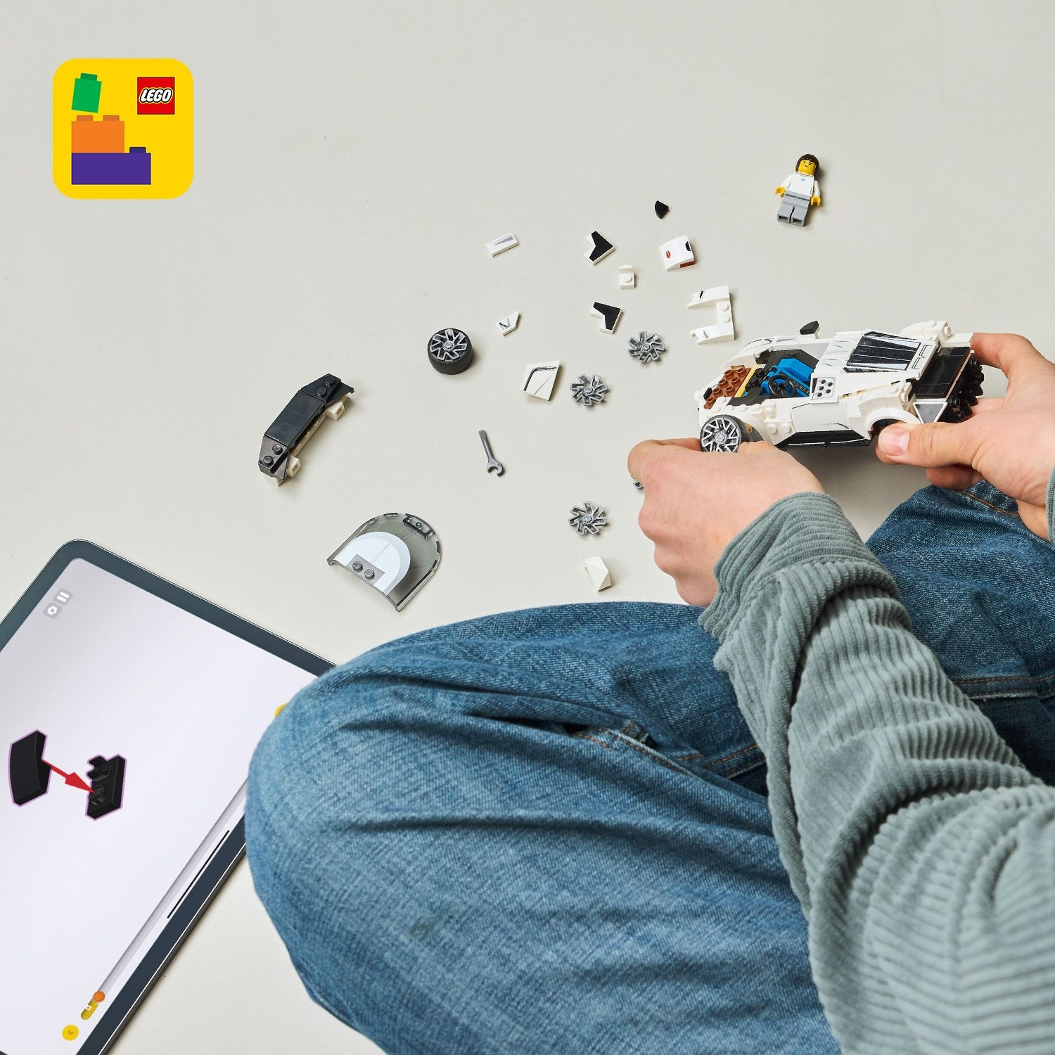 Un bambino costruisce un'auto Lego bianca con istruzioni su un tablet.