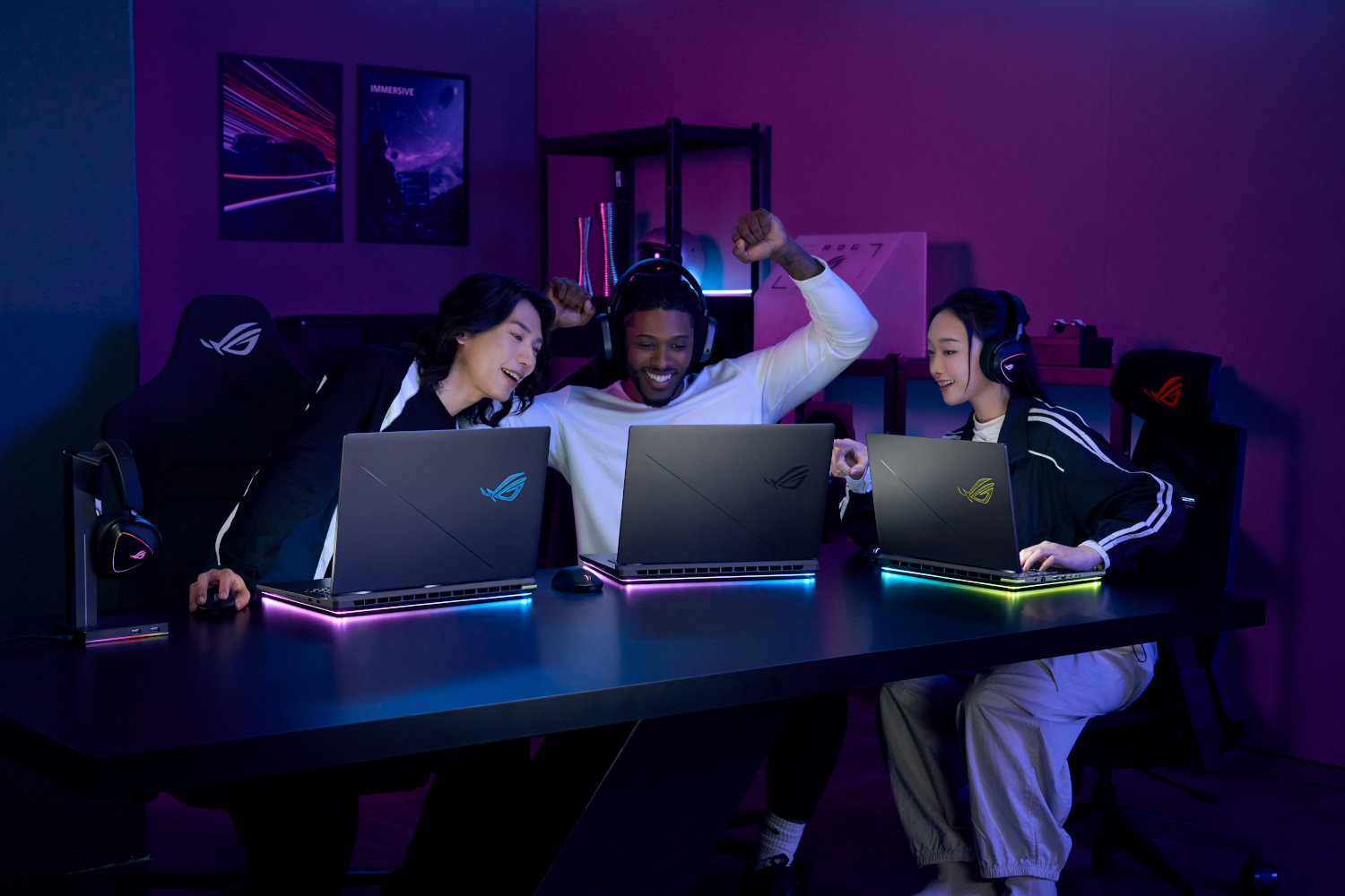 Three gamers, two women and one man, react excitedly to a game on their laptops.