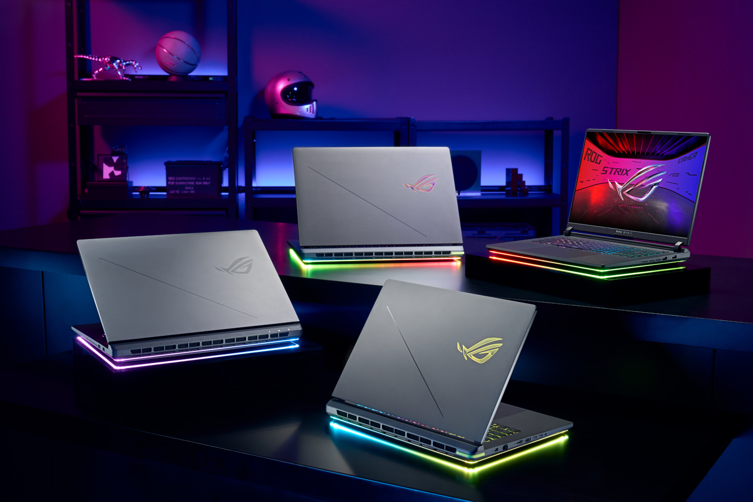 Four Asus ROG laptops with RGB lighting on dark surface. One open, three closed.