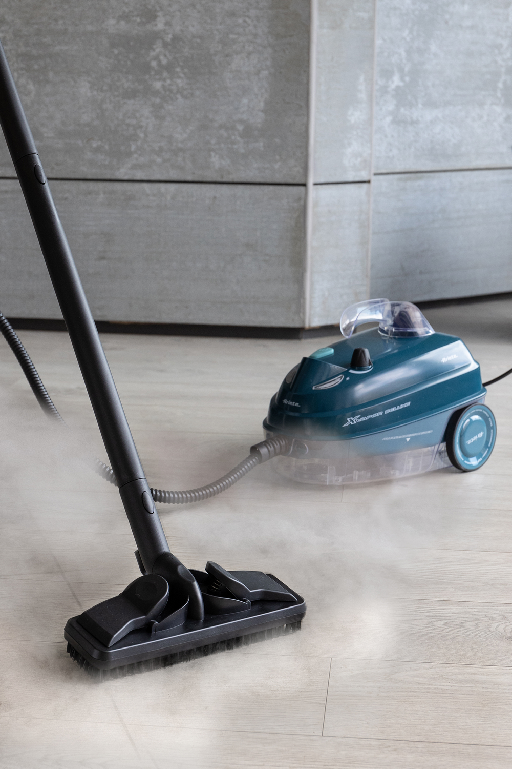 Un limpiador a vapor verde azulado con cepillo negro limpia un suelo de madera claro.