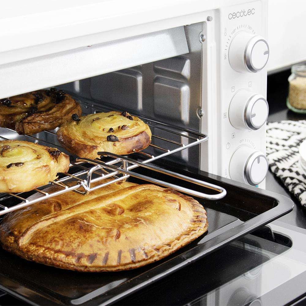 Un horno blanco con productos horneados, incluyendo un pastel grande y pasteles, en rejillas.