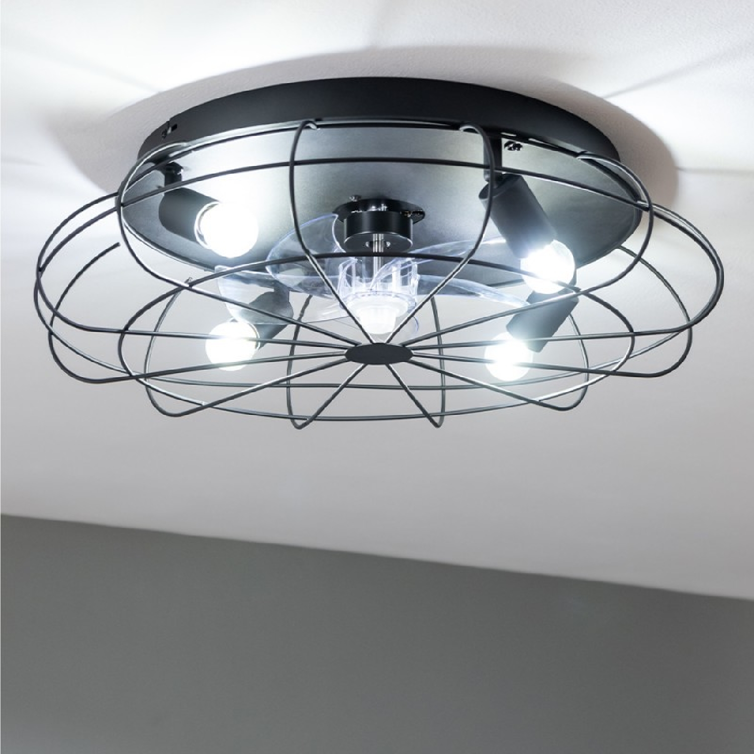 Una luz de ventilador de techo industrial negra con pantalla de metal tipo jaula y cuatro bombillas.