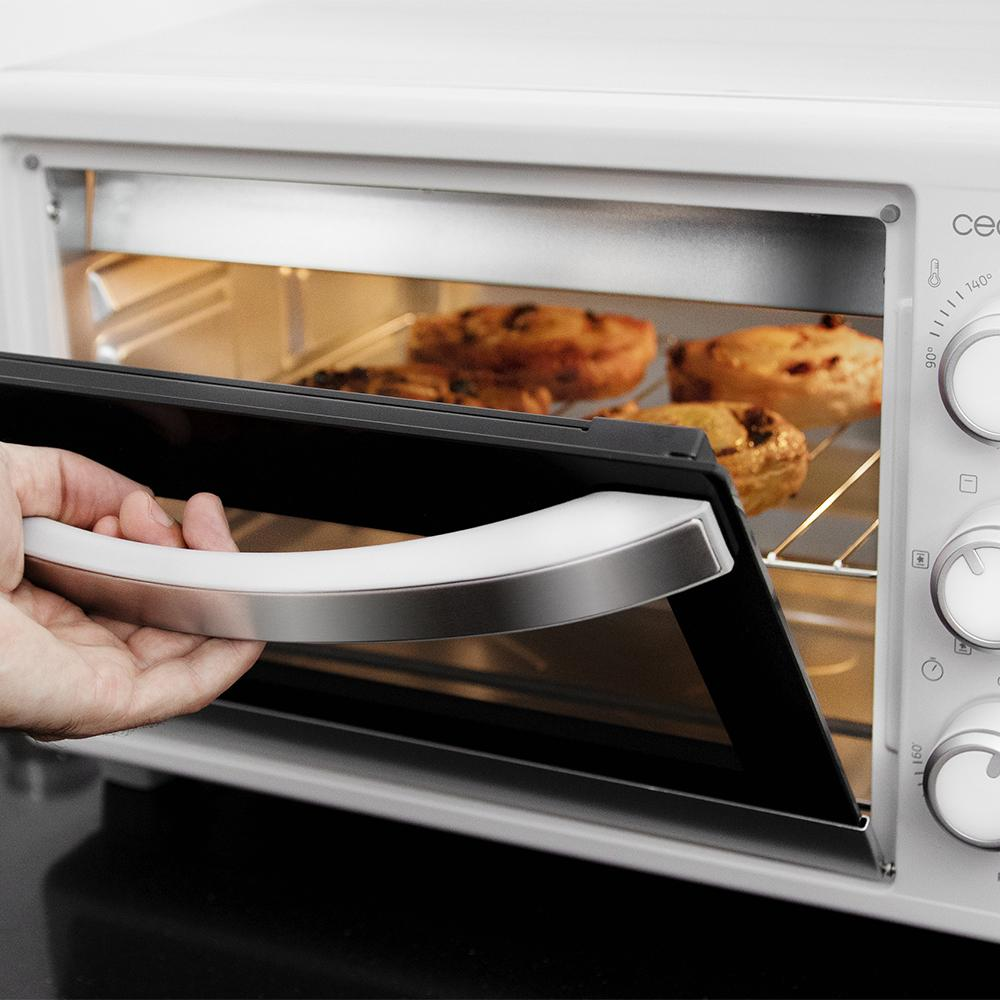 Una mano abre un horno blanco con pasteles dorados en una rejilla dentro.