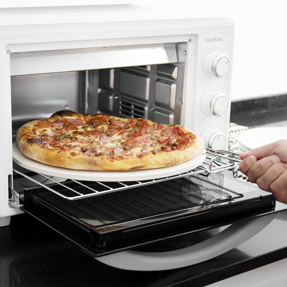 Una mano coloca una pizza cocida sobre una piedra en un horno blanco.