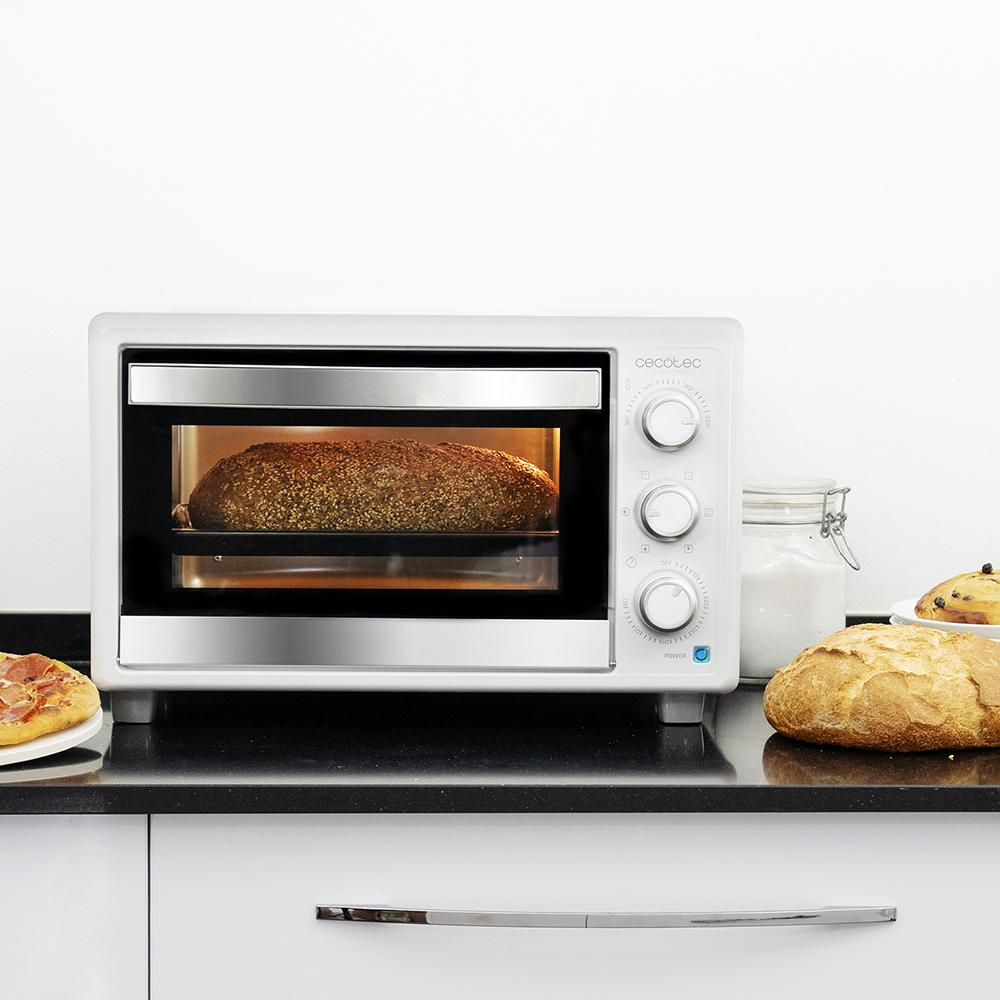 Horno blanco con una hogaza de pan dentro. A su lado hay pan, un pastel y azúcar.