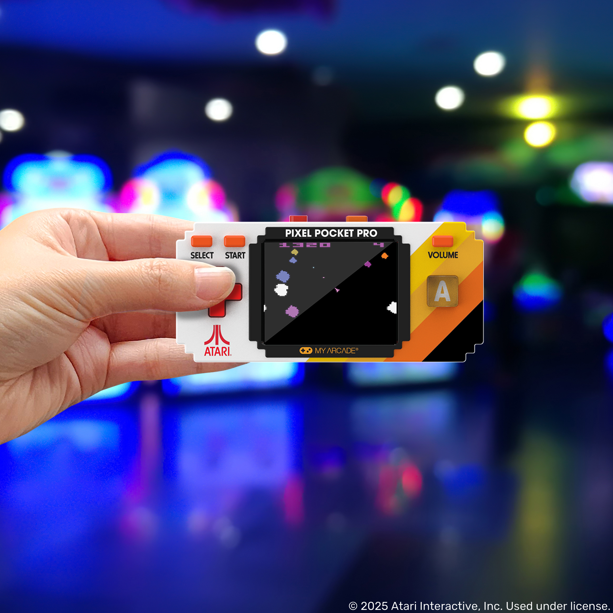 Atari logosuna sahip Pixel Pocket Pro taşınabilir oyun cihazını tutan el. Bulanık atari salonu arka planı.