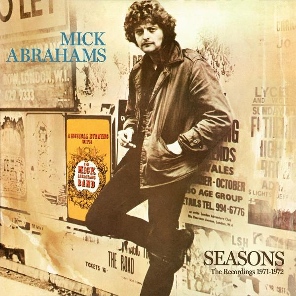 Mick Abrahams in brauner Jacke lehnt an einer Wand voller Poster und Text.