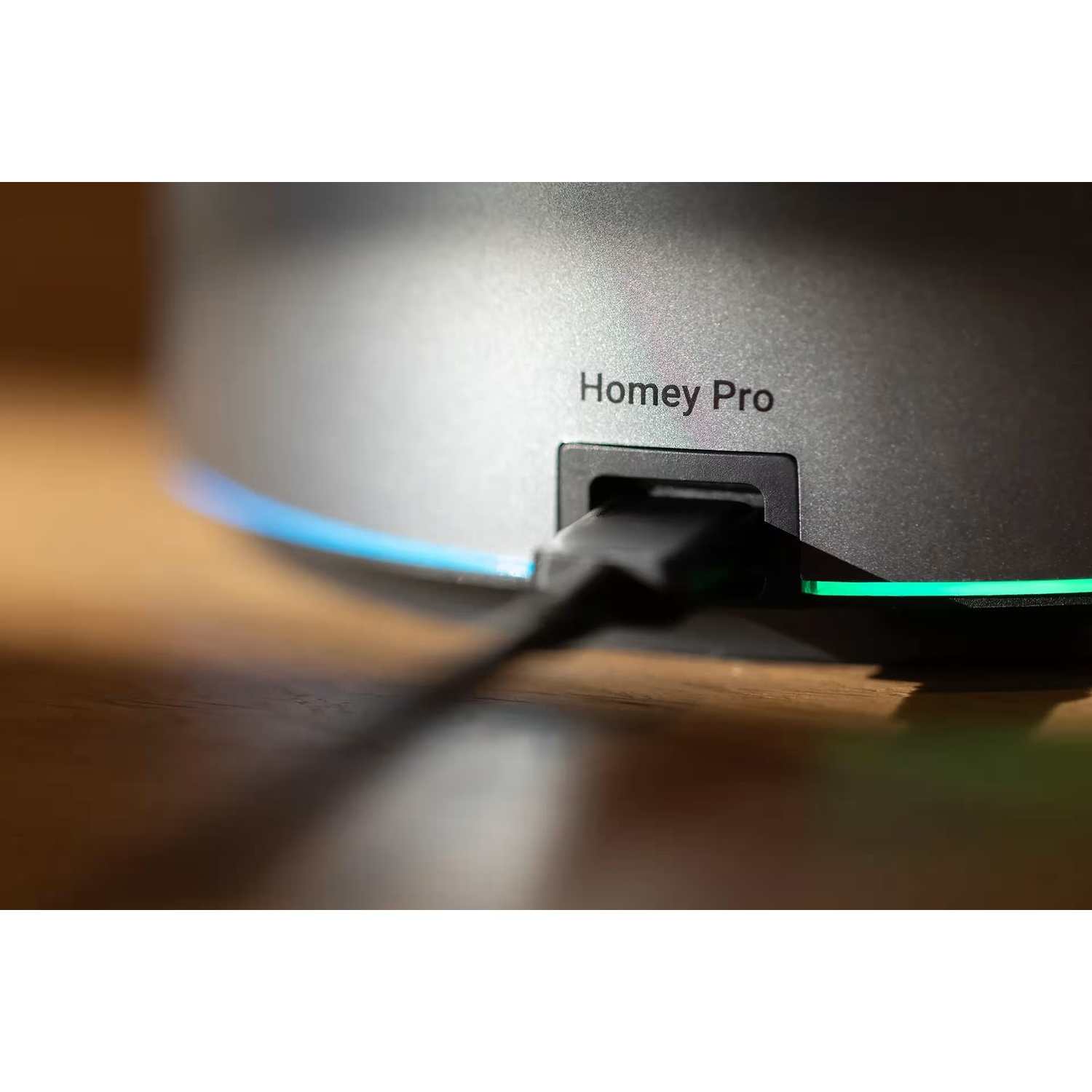 A black cable plugs into the 'Homey Pro' device, with blue and green LED lights.