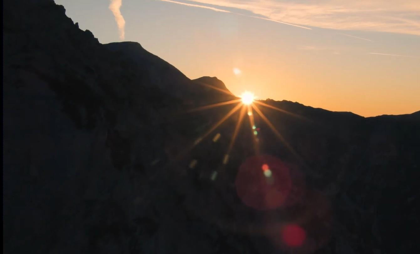 Sonnenaufgang über dunklen Bergen mit Sonnenstrahlen und Kondensstreifen.