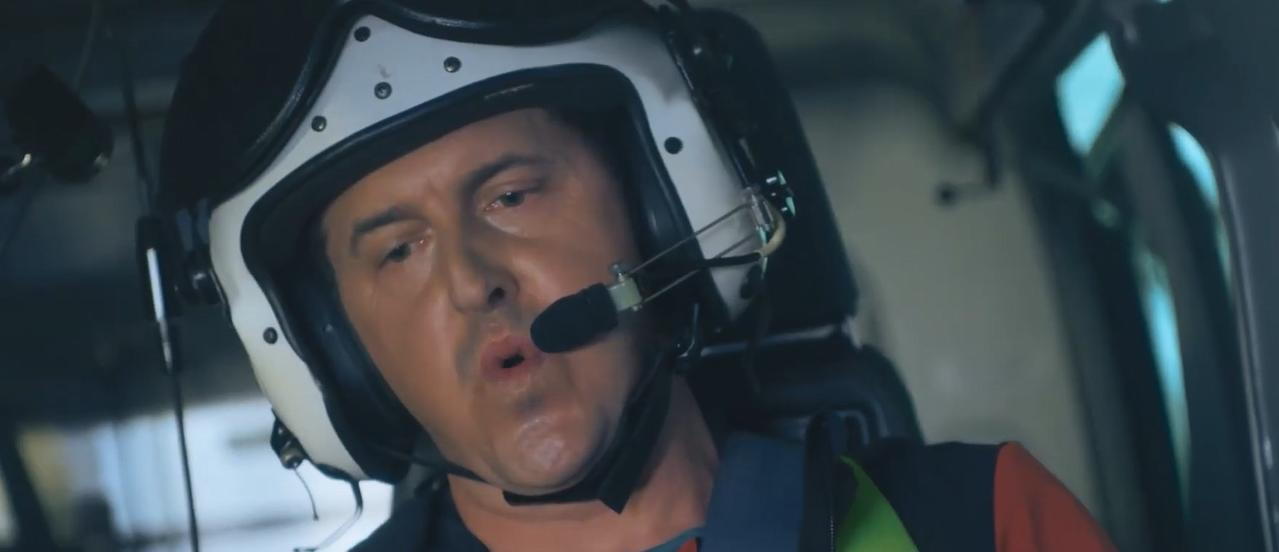 Pilot im Helm und Headset spricht in ein Mikrofon im Cockpit eines Hubschraubers.