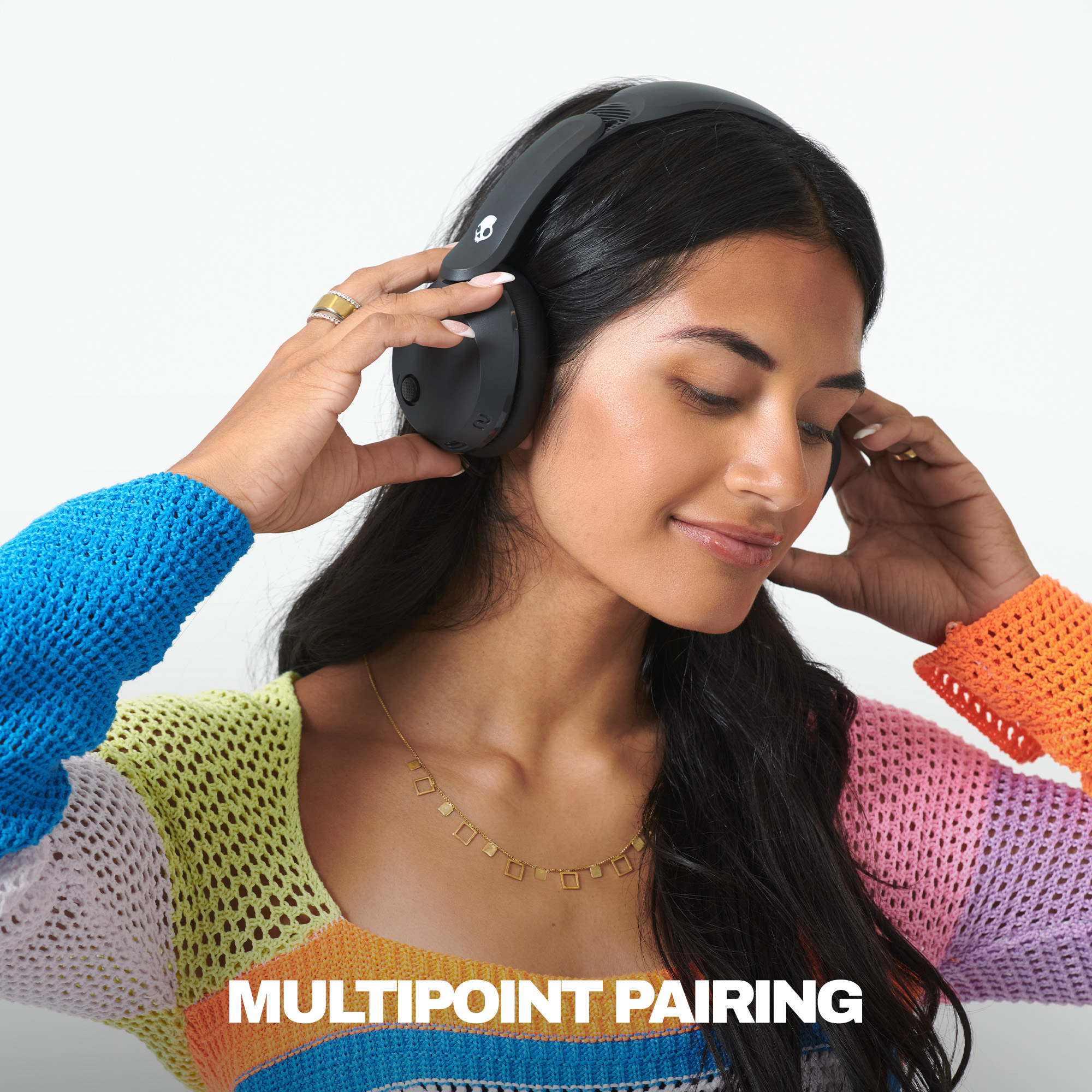 Eine Frau trägt schwarze Kopfhörer und einen bunten Häkelpullover. Text: MULTIPOINT PAIRING.