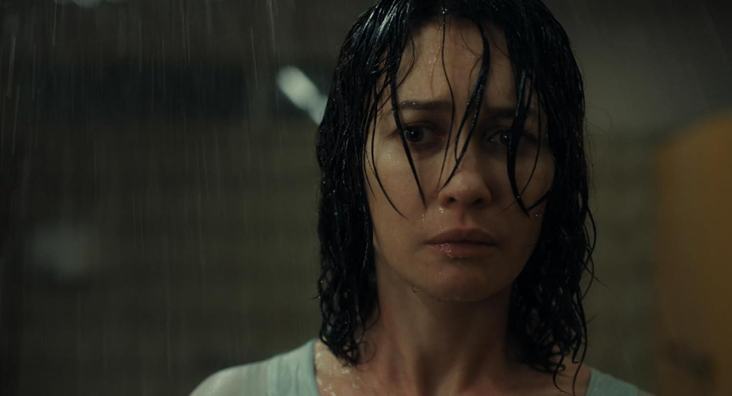 Eine Frau mit nassen Haaren blickt im Regen nach vorn. Wasser tropft ihr ins Gesicht.