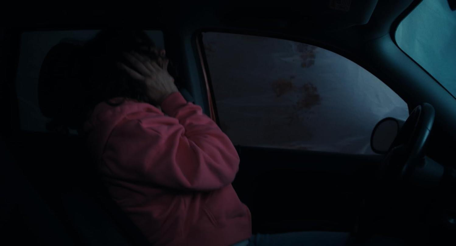 Eine Person in einem rosafarbenen Kapuzenpullover bedeckt ihr Gesicht in einem dunklen Auto.