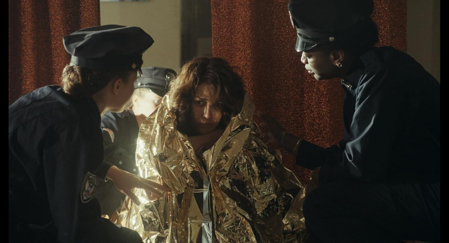Eine Frau in eine glänzende Golddecke gehüllt, umgeben von Polizisten in dunklen Uniformen.
