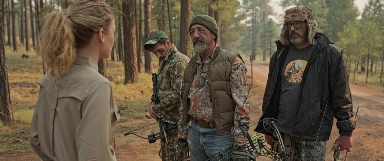 Vier Personen in Waldkleidung stehen mit Bögen im Wald.