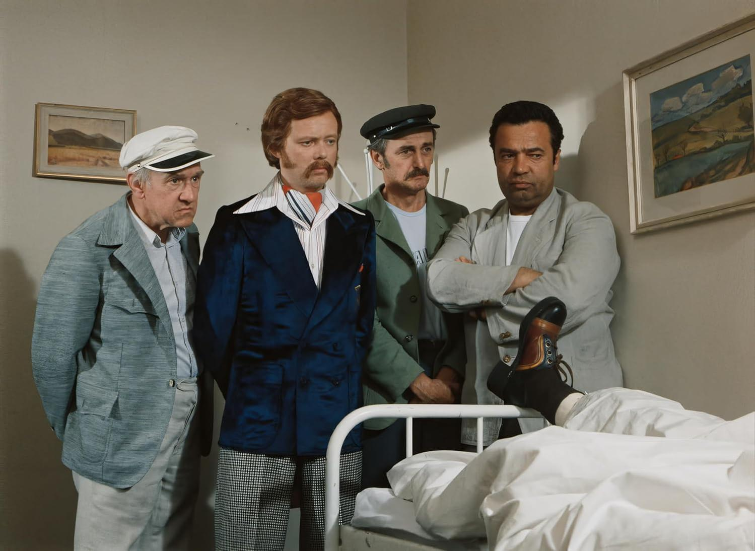 Vier Männer stehen um ein Krankenhausbett. Der Fuß eines Mannes ist auf dem Bett sichtbar.